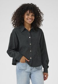 Schwarzes Denim-Hemd mit Kragen, silbernen Knöpfen und hochgekrempelten Ärmeln, kombiniert mit hellblauen Jeans.