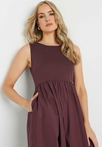 El vestido sin mangas de color burdeos presenta un escote redondo y una cintura fruncida. Fabricado con una tela suave y liviana, tiene un corte holgado y bolsillos laterales.