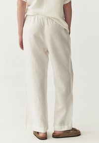 Bílé lněné kalhoty s volným střihem, s elastickým pasem a širokými nohavicemi. V kombinaci s hnědými sandály. Minimalistický design.