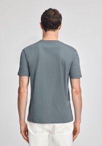 Grå t-shirt med kort ärm och rund halsringning, slät textur och slim fit, visad bakifrån med vita byxor.