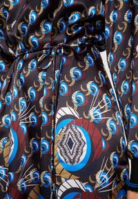 Tissu à motif présentant des couleurs vives : noir avec des formes bleues, rouges et dorées. Inclut un détail de taille nouée et une texture fluide.