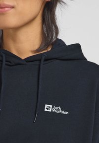 Felpa con cappuccio blu navy con texture a coste; presenta un logo bianco di Jack Wolfskin sul davanti e coulisse per la regolazione.