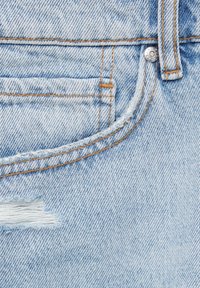 Vaaleansinisiä farkkuja, joissa on kulutettu alue, kontrastoiva oranssiompelu ja klassinen viiden taskun muotoilu, jossa on metallinen nappi.