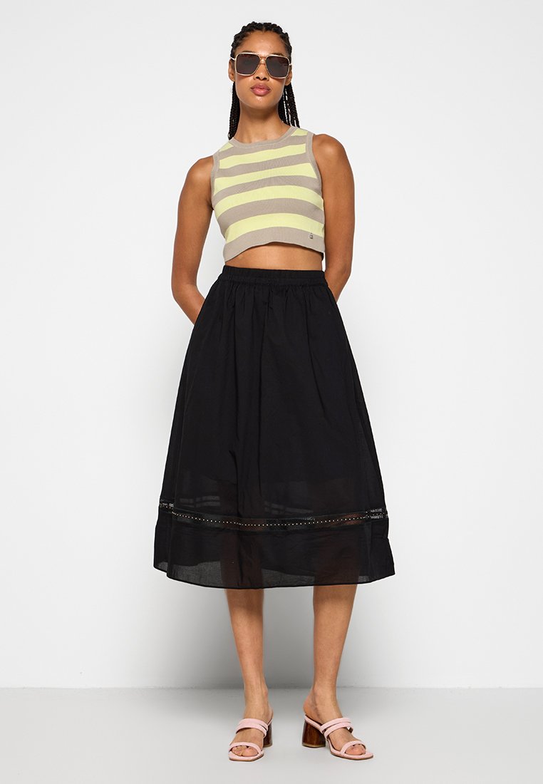 Beżowy i żółty wzorzysty crop top w połączeniu z czarną, luźną, długości kostek spódnicą z teksturowanym dołem i subtelnymi zdobieniami.