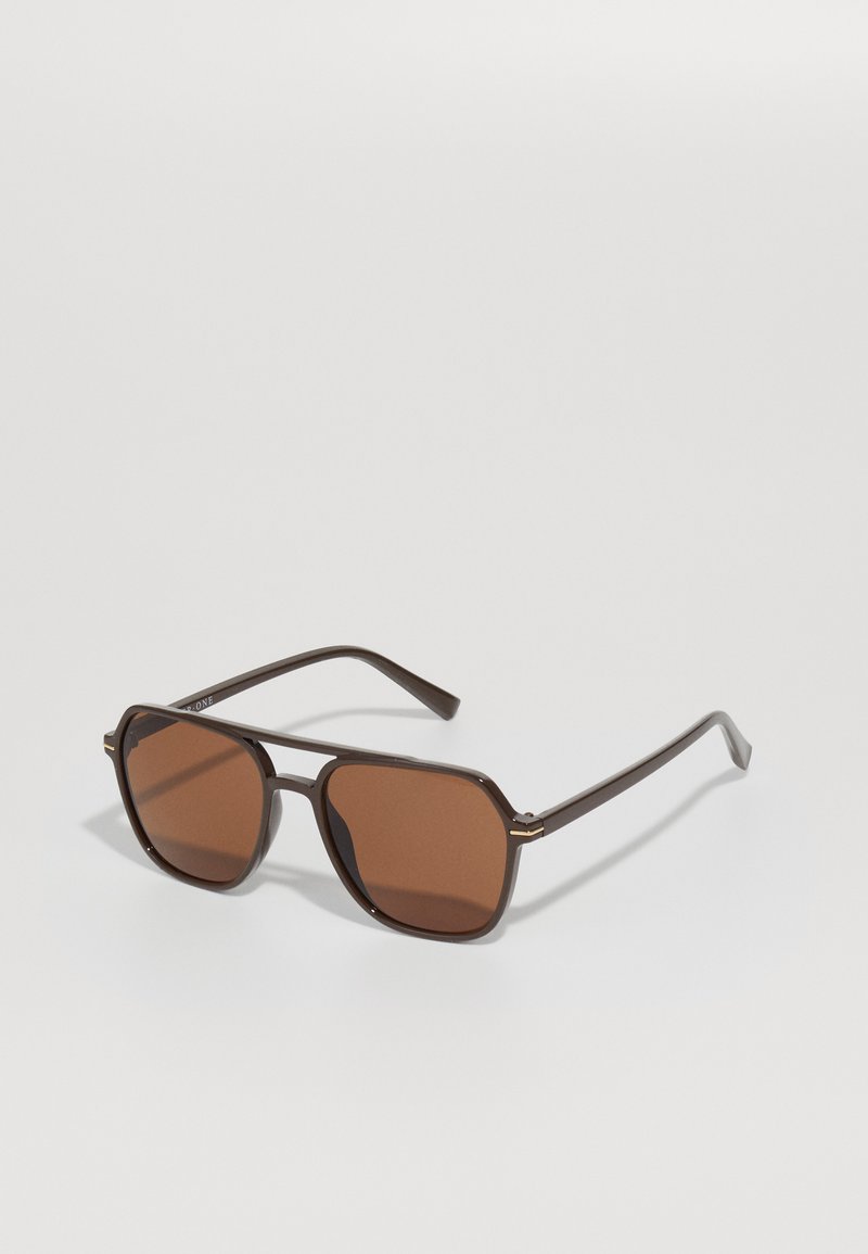 Brown sunglasses with a geometric frame, featuring rich brown lenses and thin metal accents on the temples, set against a neutral background.