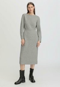 Vestito grigio a coste con maniche lunghe e scollatura a barca, che arriva a metà polpaccio. Abbinato a stivali neri in pelle alla caviglia.