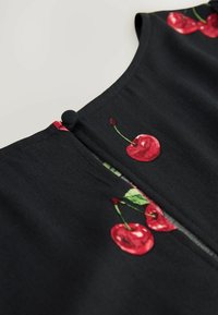 Černý top z látky s vyšitými červenými třešněmi a zelenými listy, s výstřihem ve tvaru klíčky a detaily s knoflíkovým zapínáním.
