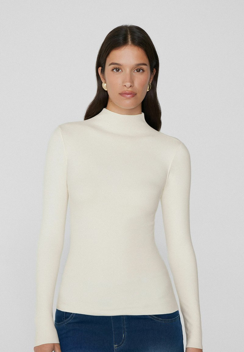 Witte langemouwen top met een hoge nek; aansluitend ontwerp van soepel materiaal. Kenmerkt zich door een naadloze, minimalistische stijl.