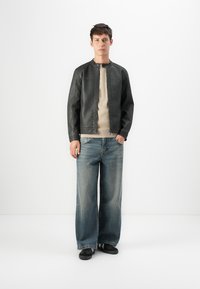 Veste en cuir noire avec un col rond, des manches texturées, une chemise beige clair en dessous et un jean denim à jambes larges.