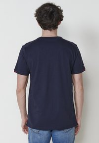 Tumši zila kokvilnas T-kreklu ar īsām piedurknēm, apaļu kakla izgriezumu un svītrām uz piedurkņu malām. Vienkāršs aizmugures skats, brīvi iekļauts.