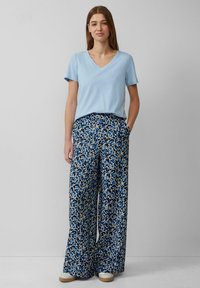 Lichtblauwe V-hals t-shirt gecombineerd met wijde, gemusterde broek in blauw, crème en zwart geometrisch patroon; voorzien van zijzakken.