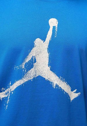 Blauw katoenen T-shirt met een grote witte silhouetafbeelding van een springende figuur die een basketbal vasthoudt. Soepele textuur, ronde hals.