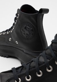 Bottes hautes Converse All Star en cuir noir avec lacets, œillets métalliques, semelles robustes et patch logo embossé à la cheville.