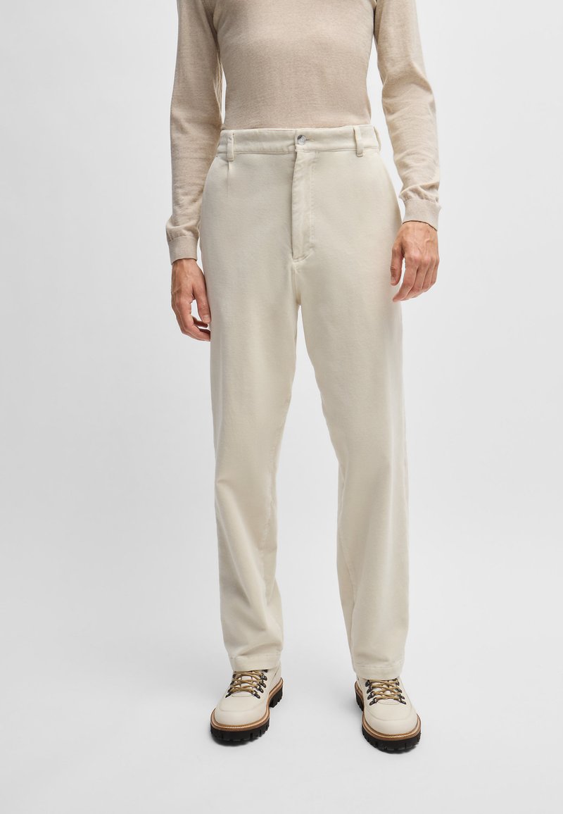 Pantalons couleur crème à coupe décontractée, dotés d'une fermeture éclair, de deux poches avant et d'un tissu légèrement texturé. Assortis à des bottes beiges à lacets.