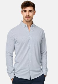 Weißes Hemd mit blauen Punkten, lange Ärmel und klassischem Kragen. Der Stoff wirkt glatt und hat einen taillierten Schnitt.