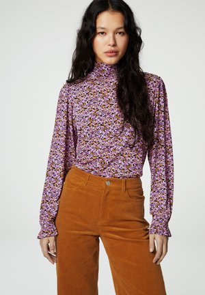 Langsleeve, hoge hals top met een paarse bloemenprint; gecombineerd met oranje corduroy broek met voorzakken en een metalen knoopdetail.