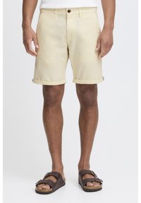Khaki shorts gemaakt van een gestructureerde stof, met opgerolde cuffs, een sluiting met een voorknop en zijzakken, gecombineerd met bruine sandalen.