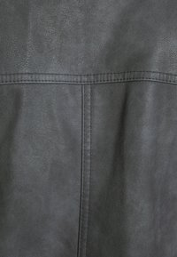 Czarna tkanina z sztucznej skóry o teksturowanej powierzchni, z widocznym szwem wzdłuż szwu i gładkim wykończeniem.