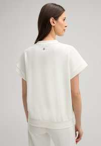 Witte korte mouwen pullover met een relaxte pasvorm, voorzien van een subtiele logo-accent bij de achterkant van de halslijn en een zachte, gladde textuur.