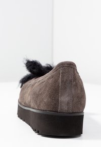 Zapato de ante marrón tipo slip-on con un acento negro suave en la parte superior, suela baja de goma y detalles de costura a lo largo de los bordes.