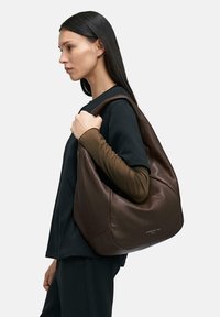 Brązowa skórzana torba na ramię o luźnym fasonie, z gładką fakturą i subtelnym logo na podstawie.