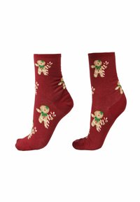 Calzini alla caviglia rossi con motivo ripetuto di omini di pan di zenzero che tengono una caramella a bastoncino, disposti fianco a fianco su uno sfondo bianco.