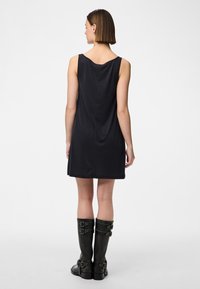 Μαύρο αμάνικο φόρεμα με απλή σιλουέτα, διαθέτοντας στρογγυλή πλάτη, συνδυασμένο με ψηλές μαύρες δερμάτινες μπότες με διακοσμητικά κούμπωμα.