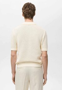 Gebreid poloshirt met korte mouwen in pale cream, met een gestructureerd patroon en een geribde kraag. Gestyled met lichte broek.