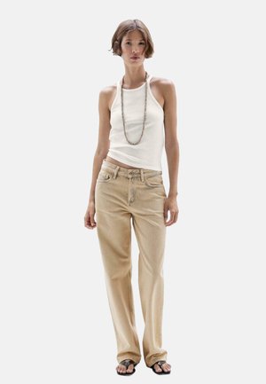 Top in cotone bianco a coste, jeans beige a gamba larga e infradito nere. Collana lunga con perline. Abbigliamento semplice e casual con una vestibilità comoda.