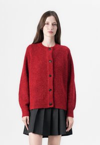 Cardigan rouge en tricot avec un col rond, des manches longues et une fermeture à boutons ; présente des boutons noirs et une finition texturée.