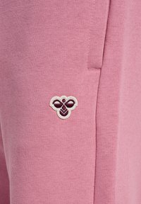 Roze joggingsbroek met een klein bijlogo geborduurd in het wit en bordeaux op de linkerkant. Het materiaal heeft een zachte, gemêleerde afwerking.