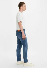 Cienkie niebieskie dżinsy z jasnym spraniem, w fasonie slim-fit, pięć kieszeni, z skórzaną metką marki na tylnej gumce. Połączone z białą koszulką i białymi trampkami.