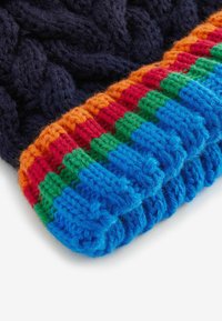 Gebreide muts met een donker marineblauw lichaam en een meerkleurige geribde rand in oranje, rood, groen en blauw met een textuurpatroon.