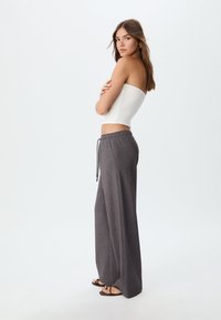 White strapless top, grey wide-leg trousers with elastic waist and drawstring, flat sandals with decorative accents, minimalistic background.
