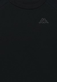 Melns īsām piedurknēm krekls, izgatavots no mīkstas auduma, ar mazu pelēku logo pie krūšu daļas. Gluda tekstūra ar apaļu kakla izgriezumu.