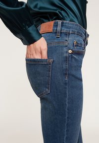 Los jeans de mezclilla en un lavado azul oscuro cuentan con un bolsillo trasero con costuras en contraste y una etiqueta de cuero marrón en la cintura.