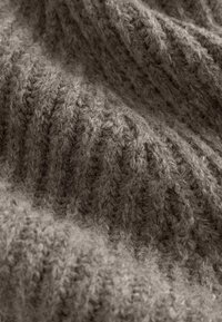 Tejido de punto marrón que muestra un patrón texturizado con acanaladuras elevadas. El material parece suave y peludo, enfatizando la calidez y la comodidad.