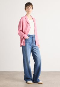 Pink relaxed button-up shirt, white tank top, wide-leg blue denim jeans, and light-colored sneakers on a model against a neutral background.
