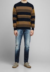 Färgglad randig tröja i marinblått och senapsgult, ribbad textur. Kombinerad med slitna ljusblå jeans och beige sneakers. Avslappnad outfit.