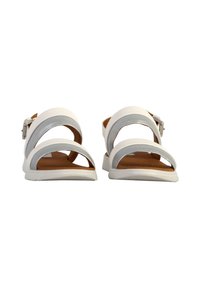 Las sandalias blancas presentan múltiples correas anchas, una hebilla en el lateral y una suela plana con un fondo texturizado. El interior es marrón.