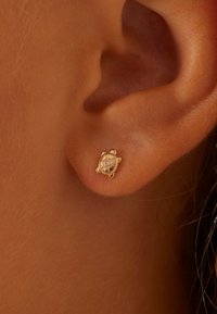 Gold stud earring with a circular design, featuring intricate detailing and a small gemstone at the center. Set in a light skin tone background.