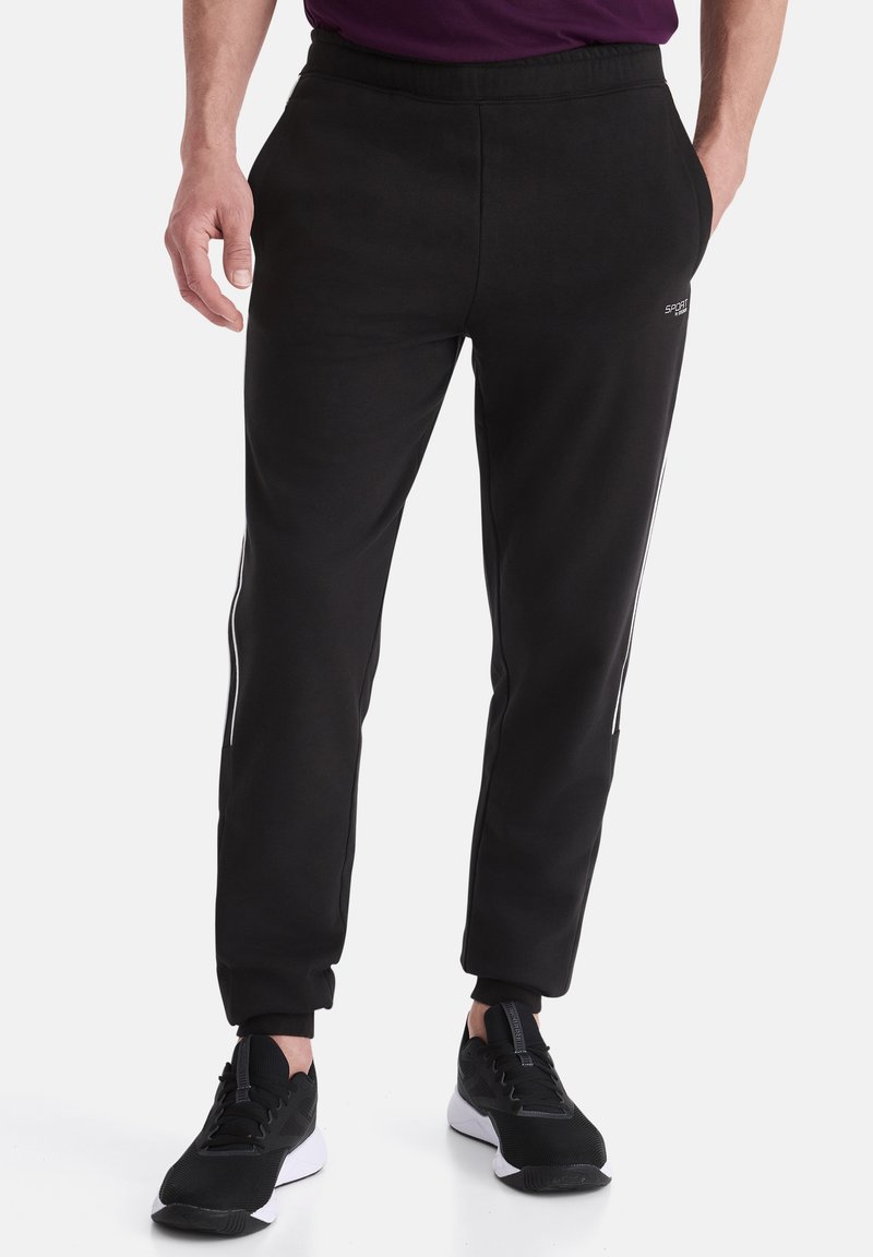 Schwarze Sweatpants aus weichem Stoff, mit schmalem Schnitt, seitlichen Streifen und einem elastischen Bund. Kombiniert mit schwarzen Sportschuhen.