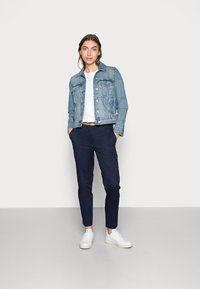 Veste en denim bleu clair, T-shirt blanc, chinos navy et baskets blanches. Éléments notables : devant boutonné, poches et longueur au niveau de la cheville.