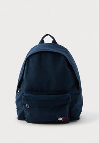 Marineblå kordfløjl rygsæk med en rund form, frontlomme med lynlås og et logo-tag. To topstropper til bæring eller ophængning.