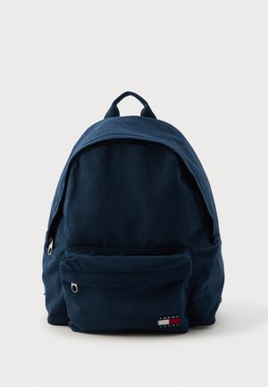 Marineblå kordfløjl rygsæk med en rund form, frontlomme med lynlås og et logo-tag. To topstropper til bæring eller ophængning.