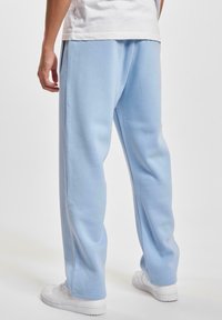 Lichtblauwe sweatpants van zachte stof, met een relaxte pasvorm en elastische tailleband, gecombineerd met witte sportschoenen.