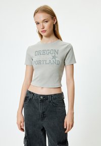 Harmaa ribattu lyhythihainen crop-top, jossa on tummanharmaa "Oregon Portland" -graafinen printti, yhdistettynä korkeavyötäröisiin mustiin farkkutaskuhousuihin.
