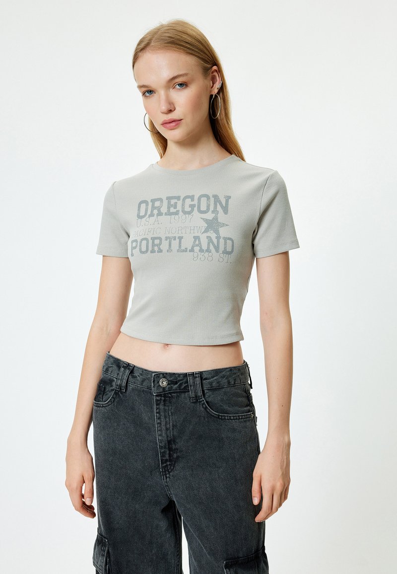 Harmaa ribattu lyhythihainen crop-top, jossa on tummanharmaa "Oregon Portland" -graafinen printti, yhdistettynä korkeavyötäröisiin mustiin farkkutaskuhousuihin.