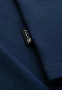 Tummansininen puuvillapaita, jolla on sileä pinta. Paidassa on pieni musta etiketti, jossa on sana "ombre" näkyvissä hihassa.