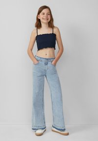 Granatowa bluzka ze marszczeniami, krótka z falbaniastymi krawędziami, w połączeniu z jasnoniebieskimi spodniami z szerokimi nogawkami i białymi trampkami z brązowymi podeszwami.